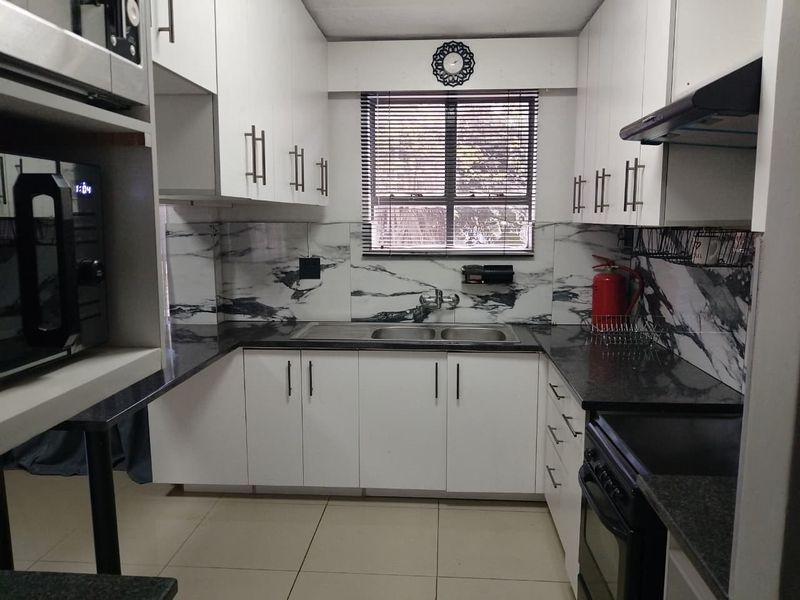 A well-maintained kitchen featuring white cabinetry, granite countertops, a marble-look splashback, and integrated appliances including an oven and extractor fan.