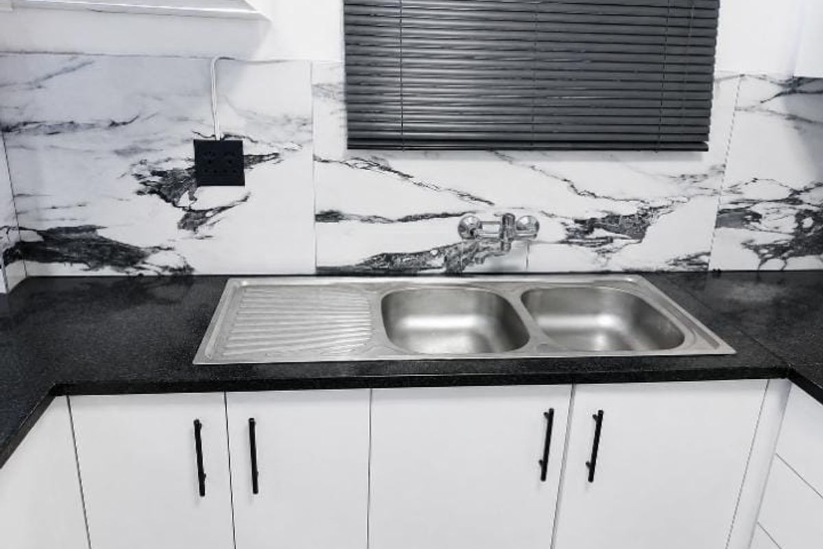 A clean, modern kitchen area featuring a stainless steel double sink, granite countertops, and marble-patterned splashback tiles.