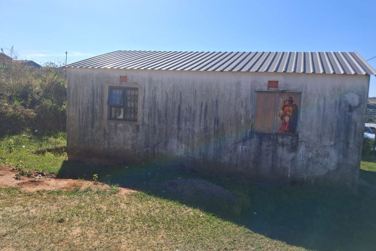 Rear view of a detached structure featuring a corrugated metal roof, security-barred windows, and significant exterior wall weathering and plaster cracking.