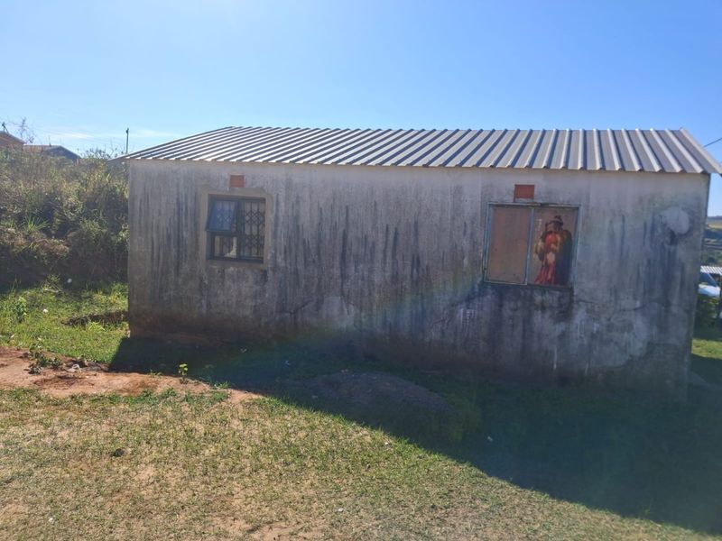Rear view of a detached structure featuring a corrugated metal roof, security-barred windows, and significant exterior wall weathering and plaster cracking.