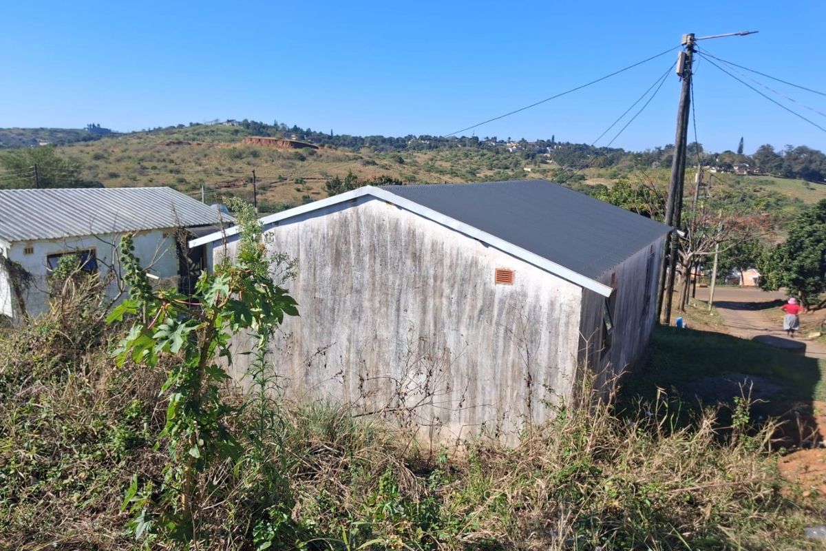 Rear view of a small residential structure featuring a corrugated metal roof and weathered exterior walls set in a rural landscape.