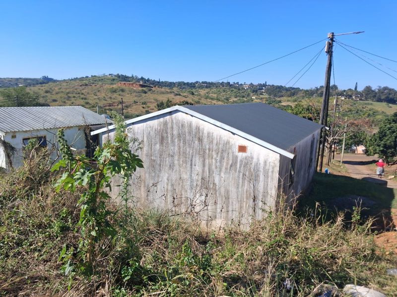 Rear view of a small residential structure featuring a corrugated metal roof and weathered exterior walls set in a rural landscape.