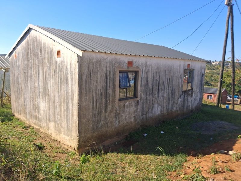 Rear view of a detached house featuring a metal roof and top-hung windows, showing significant weathering and staining on the exterior walls.