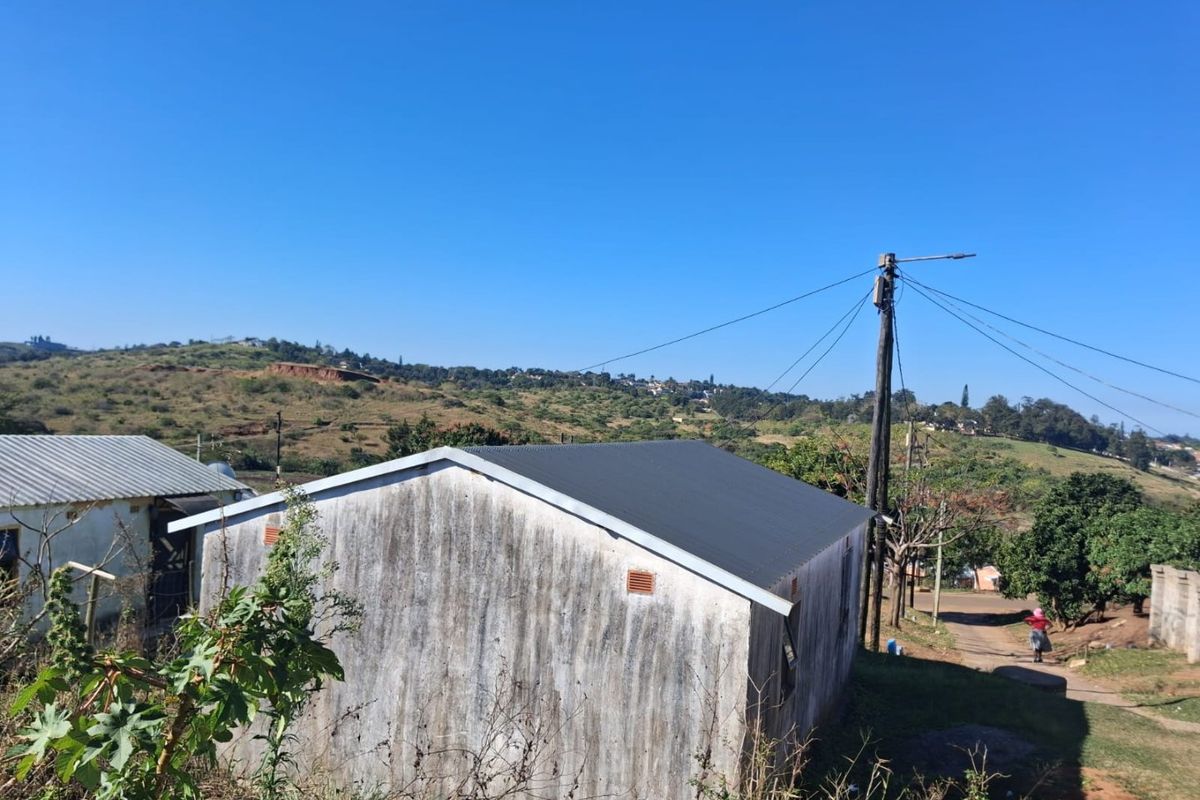 Rear view of a detached house featuring a corrugated metal roof and weathered exterior walls, situated in a rural landscape.