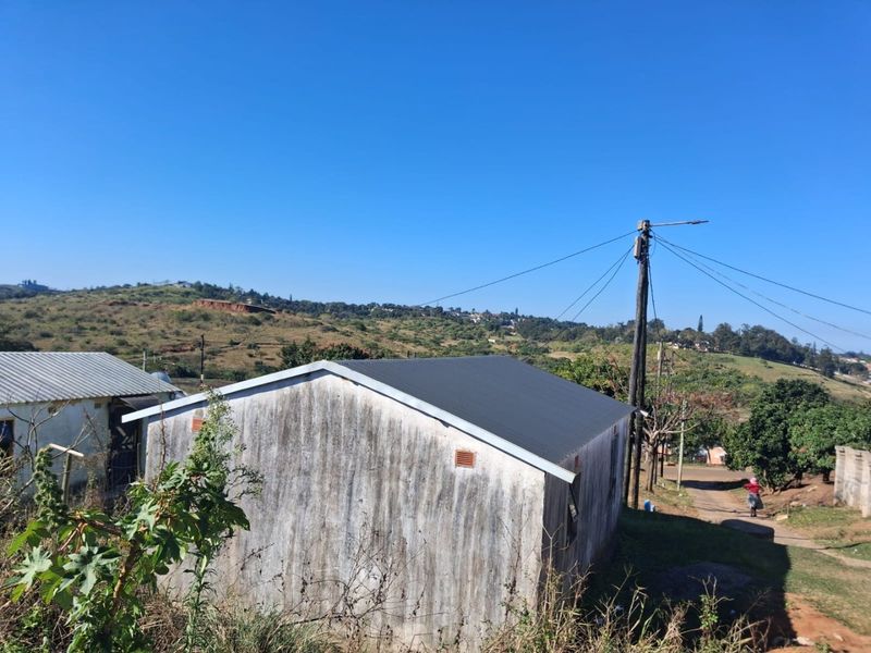 Rear view of a detached house featuring a corrugated metal roof and weathered exterior walls, situated in a rural landscape.