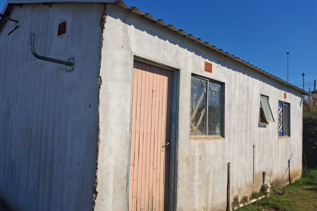 Exterior view of a basic utility structure featuring concrete walls, corrugated roofing, and external plumbing fixtures, showing signs of significant wear and maintenance needs.