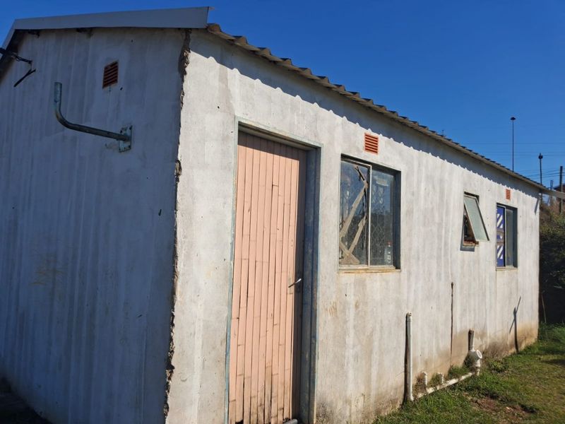 Exterior view of a basic utility structure featuring concrete walls, corrugated roofing, and external plumbing fixtures, showing signs of significant wear and maintenance needs.