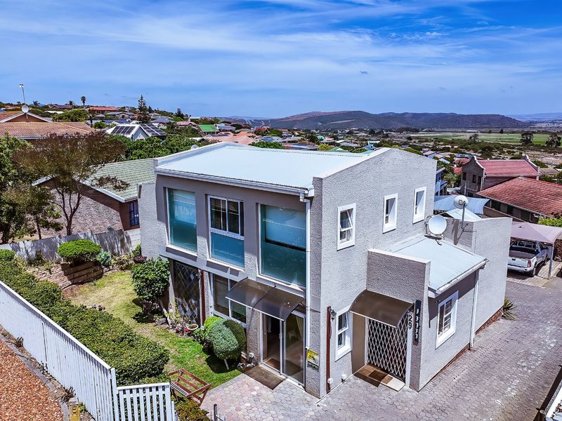 Aerial view of a two-story residential property featuring a stucco exterior, metal roof, paved driveway, and surrounding garden area in a suburban setting.