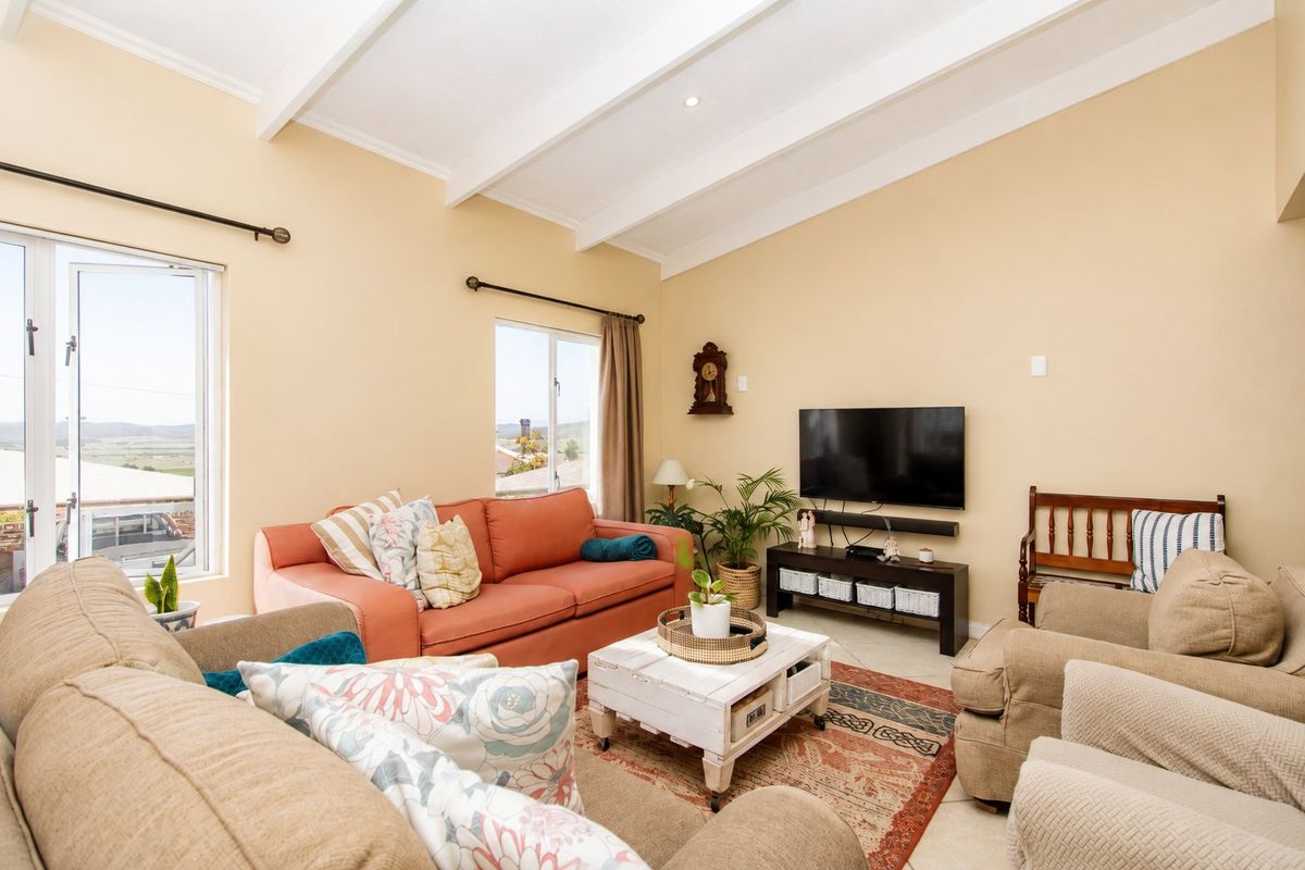 A bright living room featuring a vaulted ceiling with exposed beams, tiled flooring, and large windows providing natural light and scenic views.