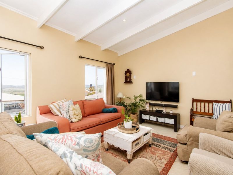 A bright living room featuring a vaulted ceiling with exposed beams, tiled flooring, and large windows providing natural light and scenic views.