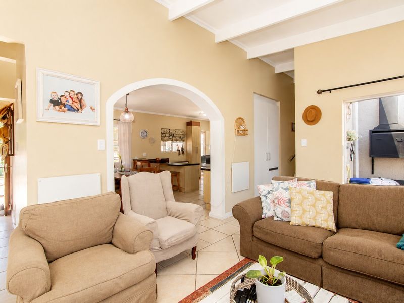 Open-plan living area featuring arched architectural details, exposed ceiling beams, and tiled flooring, with a seamless transition to the kitchen and outdoor patio area.