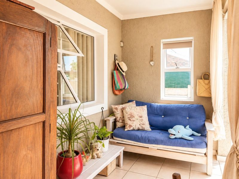 A cozy, enclosed patio area featuring tiled flooring, textured walls, and natural light through casement windows, suitable for a relaxed seating space.