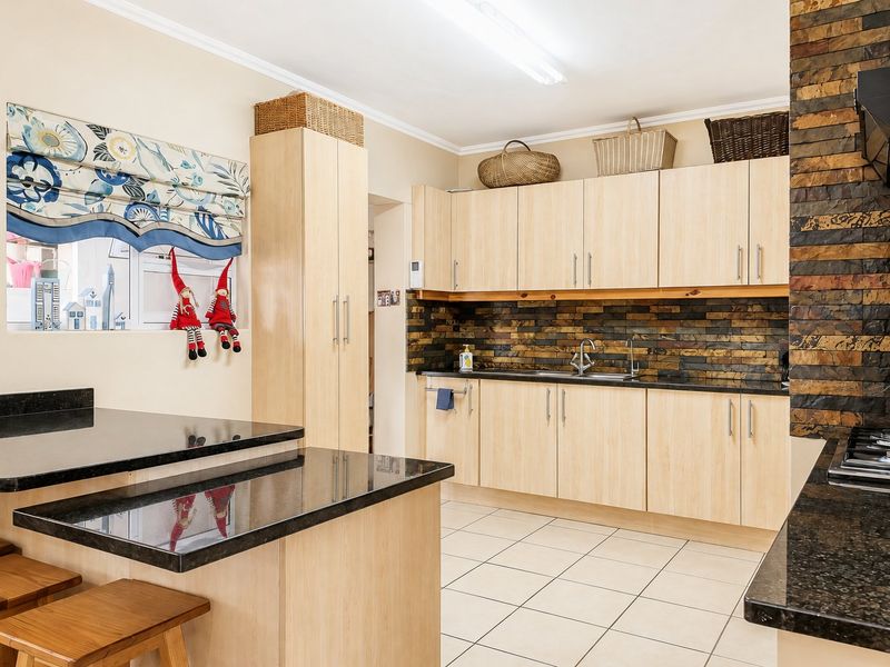 A functional kitchen featuring light wood cabinetry, dark granite countertops, a stone tile backsplash, and integrated cooking appliances with tiled flooring.