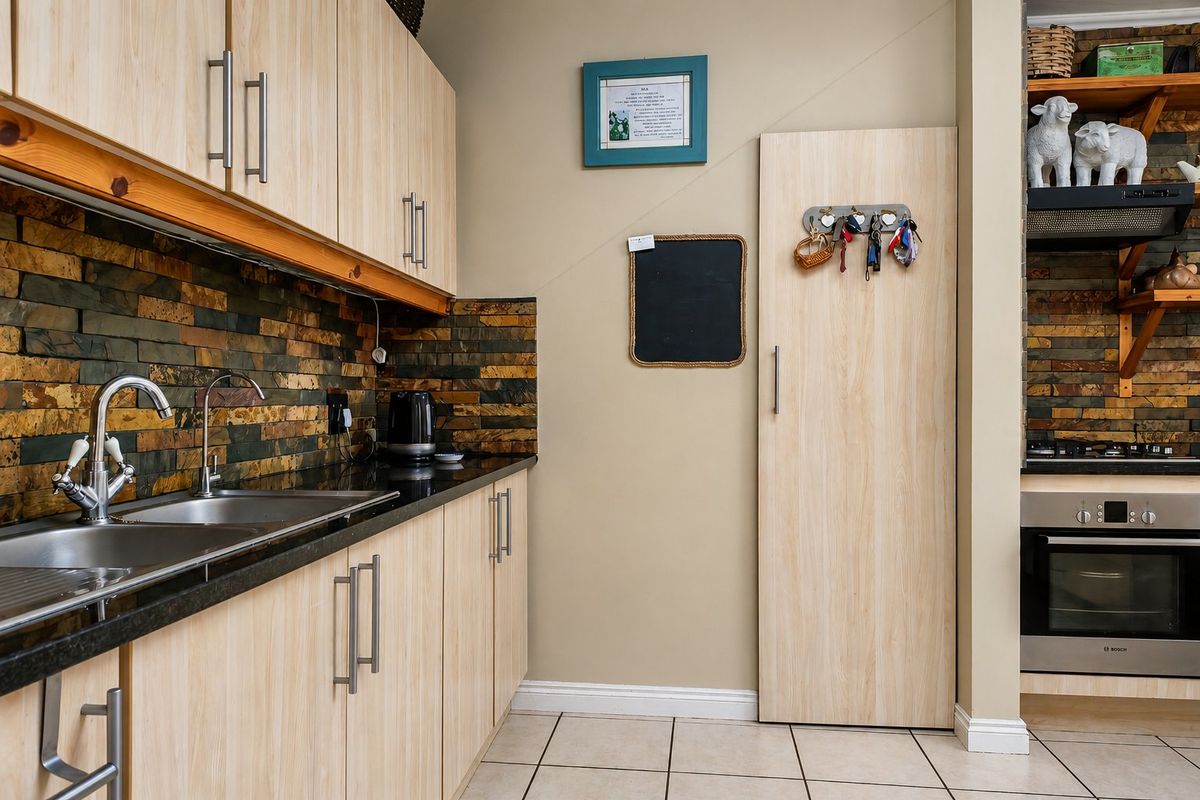 A functional kitchen featuring light wood-finish cabinetry, granite countertops, a stone tile backsplash, and integrated stainless steel appliances.