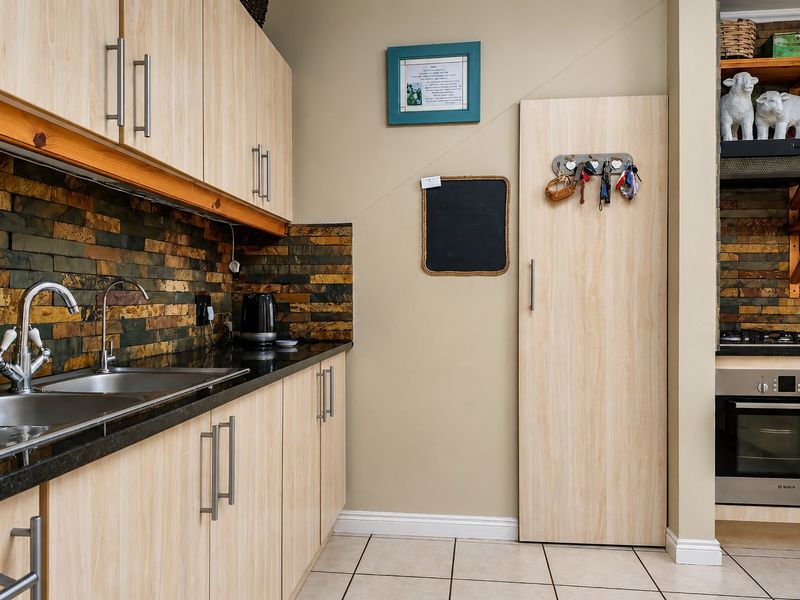 A functional kitchen featuring light wood-finish cabinetry, granite countertops, a stone tile backsplash, and integrated stainless steel appliances.