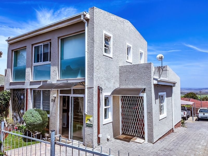 Front elevation of a two-story residential property featuring textured plaster walls, aluminium windows, security gates, and a paved driveway.