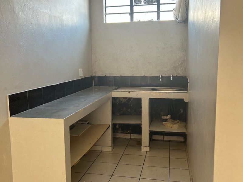 A basic scullery or utility area featuring a built-in concrete countertop, stainless steel sink, and wall-mounted electric water heater.
