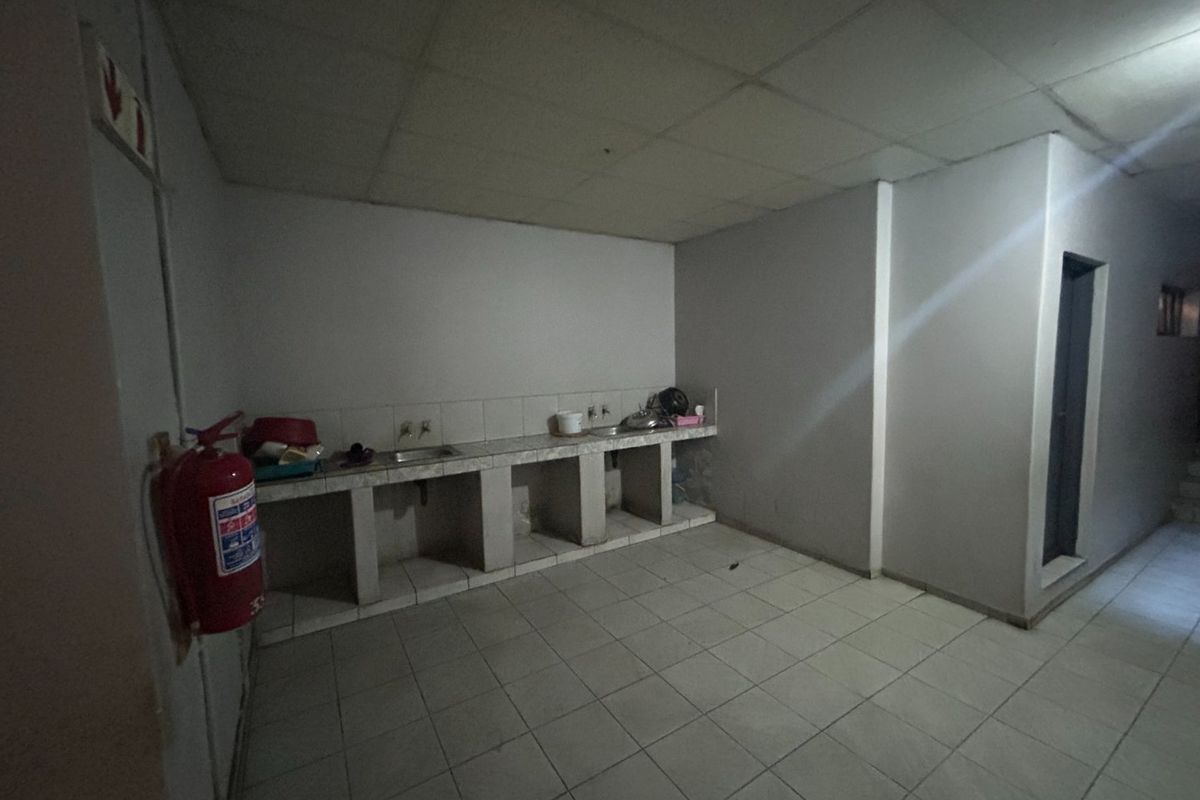 A basic, empty kitchen area featuring a tiled countertop with a built-in sink, tiled flooring, and a drop ceiling, requiring cosmetic updates.