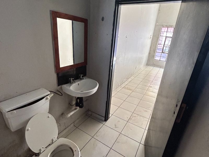 A basic bathroom featuring a toilet and pedestal basin with tiled flooring, requiring cosmetic updates and maintenance to improve its overall condition.