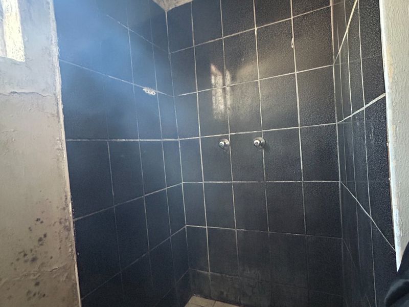 A dated shower enclosure featuring black wall tiles and a light-colored tiled floor, currently requiring significant wall repairs and cosmetic updates.