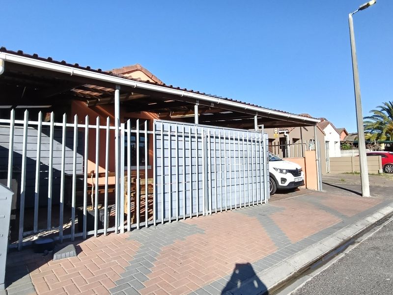 Front exterior view of the property featuring a paved driveway, covered carport, and secure steel perimeter fencing.