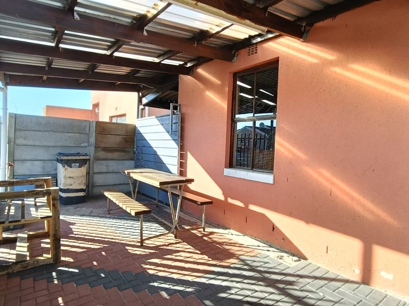 A covered outdoor patio area featuring paved flooring, a timber pergola structure, and a secure perimeter wall, suitable for outdoor dining and relaxation.