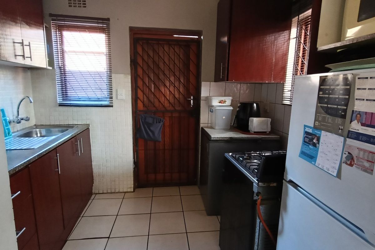 A functional kitchen featuring dark wood-look cabinetry, tiled flooring, a stainless steel sink, and a security gate leading to the exterior.