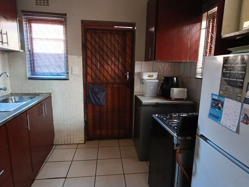 A functional kitchen featuring dark wood-look cabinetry, tiled flooring, a stainless steel sink, and a security gate leading to the exterior.