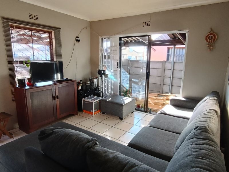 A living room featuring tiled flooring, a sliding glass door leading to the exterior, and natural light through a window with venetian blinds.