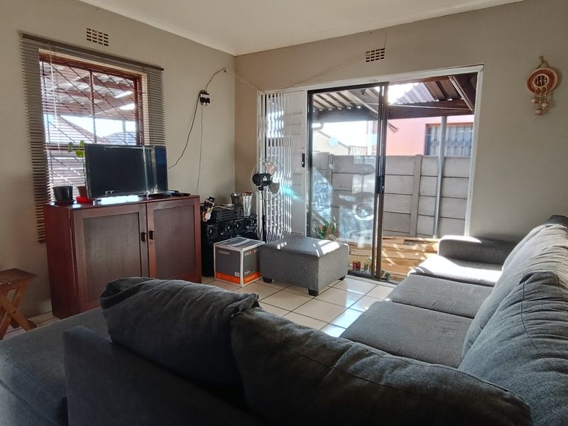 A living room featuring tiled flooring, a sliding glass door leading to an outdoor area, and a window with fitted blinds.
