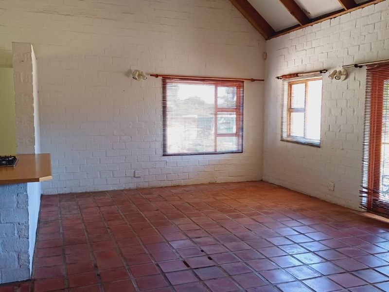 Spacious open-plan living area featuring a high vaulted ceiling with exposed timber rafters, painted brick walls, and terracotta tile flooring.