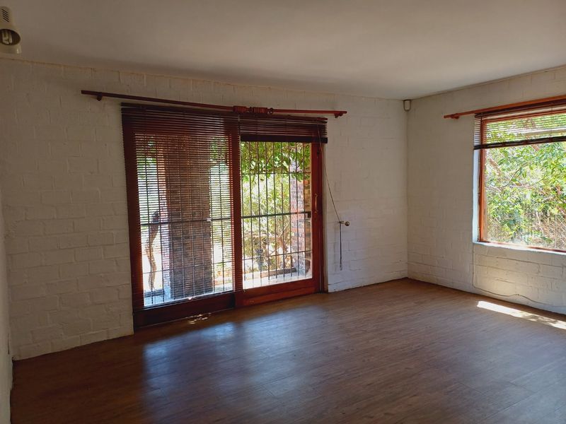 An empty living room featuring painted brick walls, laminate flooring, and a sliding glass door with security gate leading to the garden.