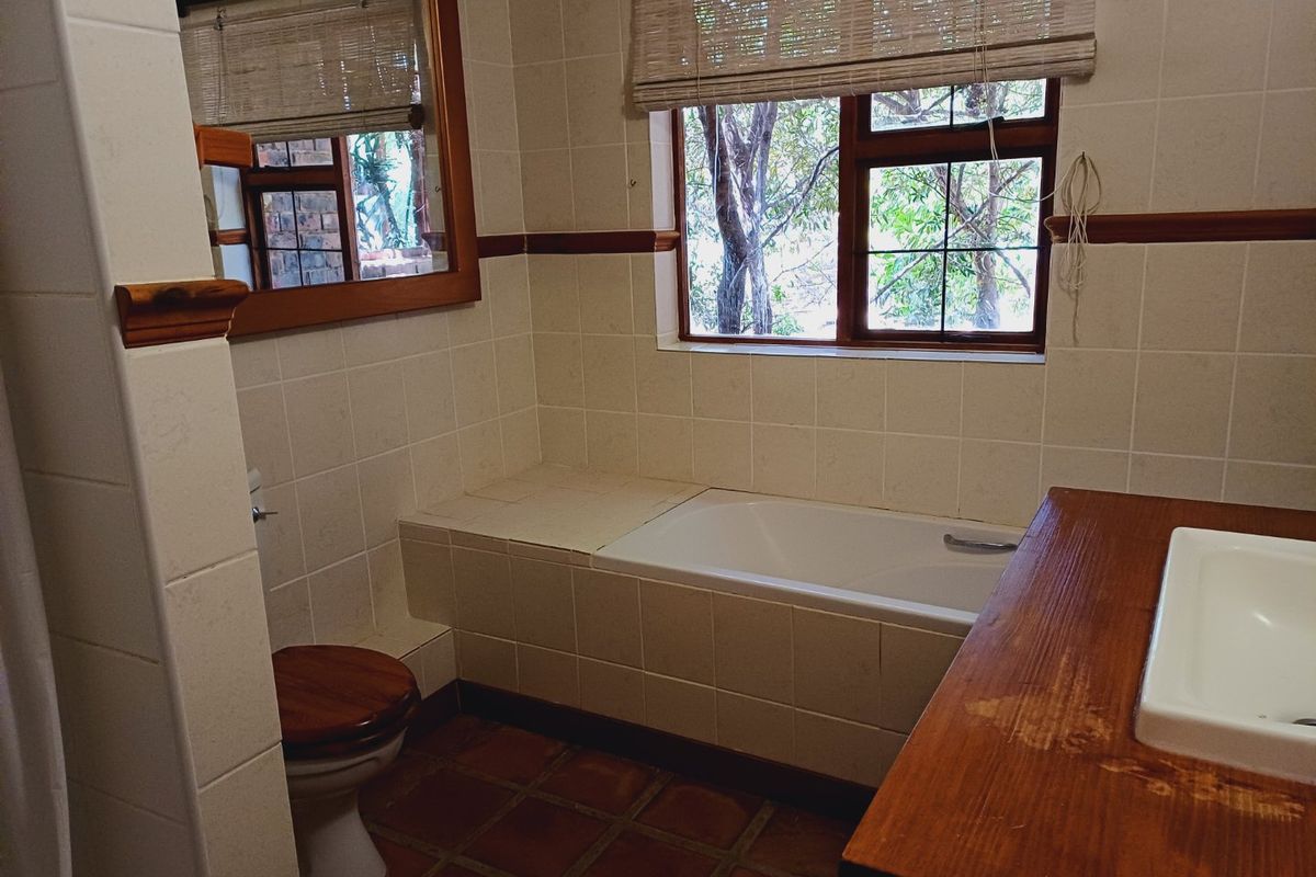 A functional bathroom featuring a built-in bathtub, tiled finishes, a wooden vanity with an inset basin, and a toilet, with natural light from the window.