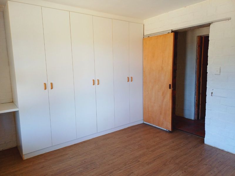 A clean, empty bedroom featuring extensive white built-in cupboards, warm-toned laminate flooring, and a sliding wooden door leading to an adjacent space.