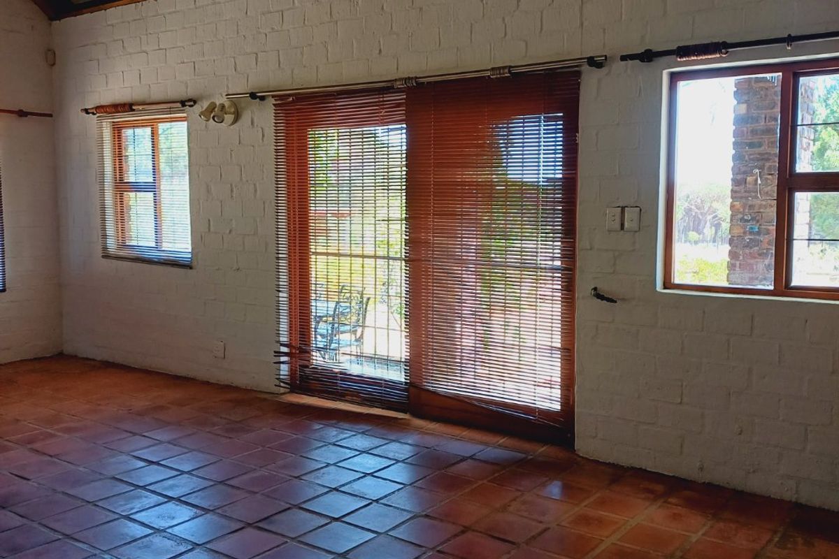 Spacious living area featuring high vaulted ceilings with exposed timber rafters, terracotta tile flooring, and large windows providing natural light and garden access.