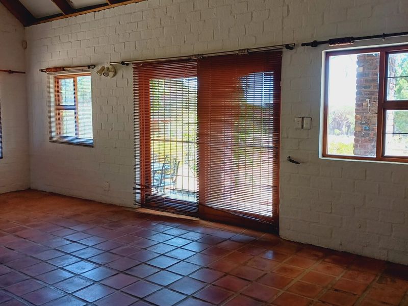 Spacious living area featuring high vaulted ceilings with exposed timber rafters, terracotta tile flooring, and large windows providing natural light and garden access.