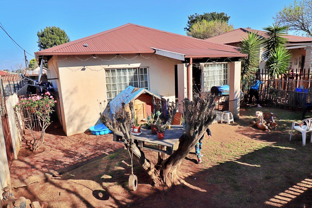 Rear view of the property featuring a corrugated metal roof, brick paved area, and perimeter fencing.