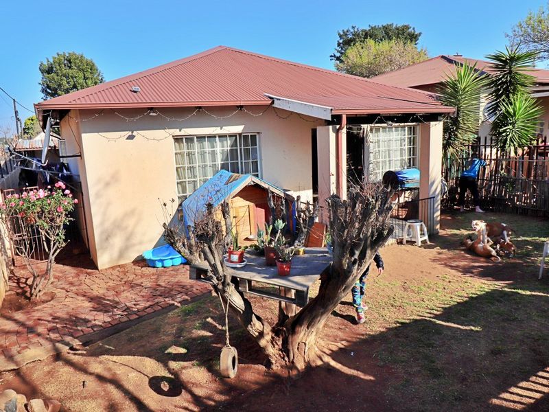 Rear view of the property featuring a corrugated metal roof, brick paved area, and perimeter fencing.