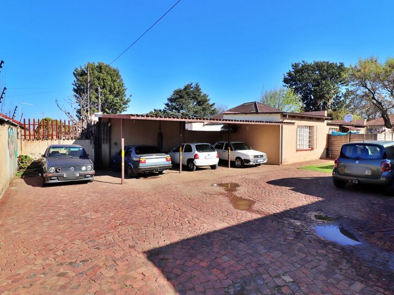 Rear exterior view featuring a paved driveway, a covered carport structure, and perimeter walling with electric fencing.