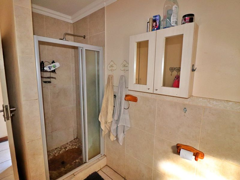A functional bathroom featuring a tiled shower enclosure, wall-mounted storage cabinet, and neutral wall tiling throughout.