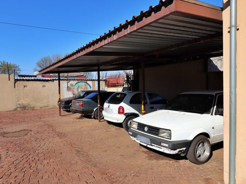 A covered carport area featuring a corrugated metal roof supported by steel posts, situated over a brick-paved driveway.