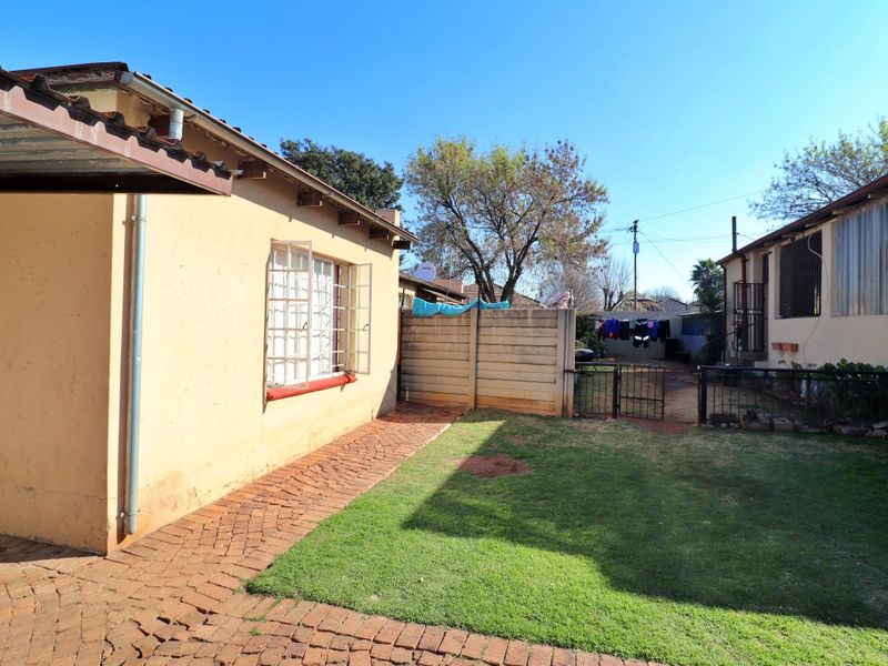 Rear exterior view of the property featuring a small lawn, brick paved walkway, precast boundary wall, and security bars on windows.