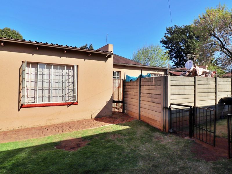 Rear exterior view of the property featuring a paved walkway, lawn area, and secure boundary walling with metal gate access.