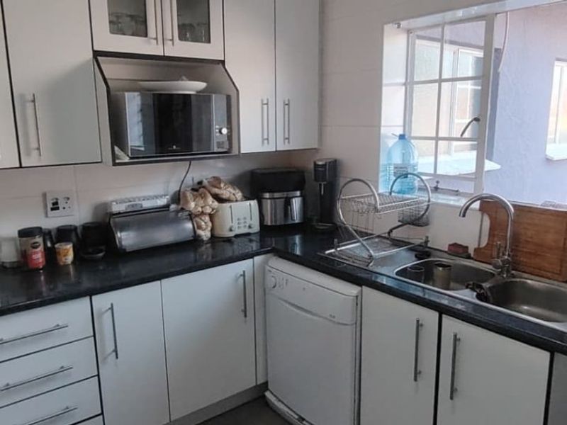 A functional kitchen featuring white cabinetry, dark countertops, a double basin sink, and tiled splashbacks with a window overlooking the exterior.