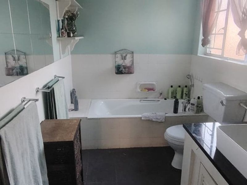 A functional bathroom featuring a built-in bathtub, vessel sink with granite vanity, and tiled finishes, offering a dated but practical layout.