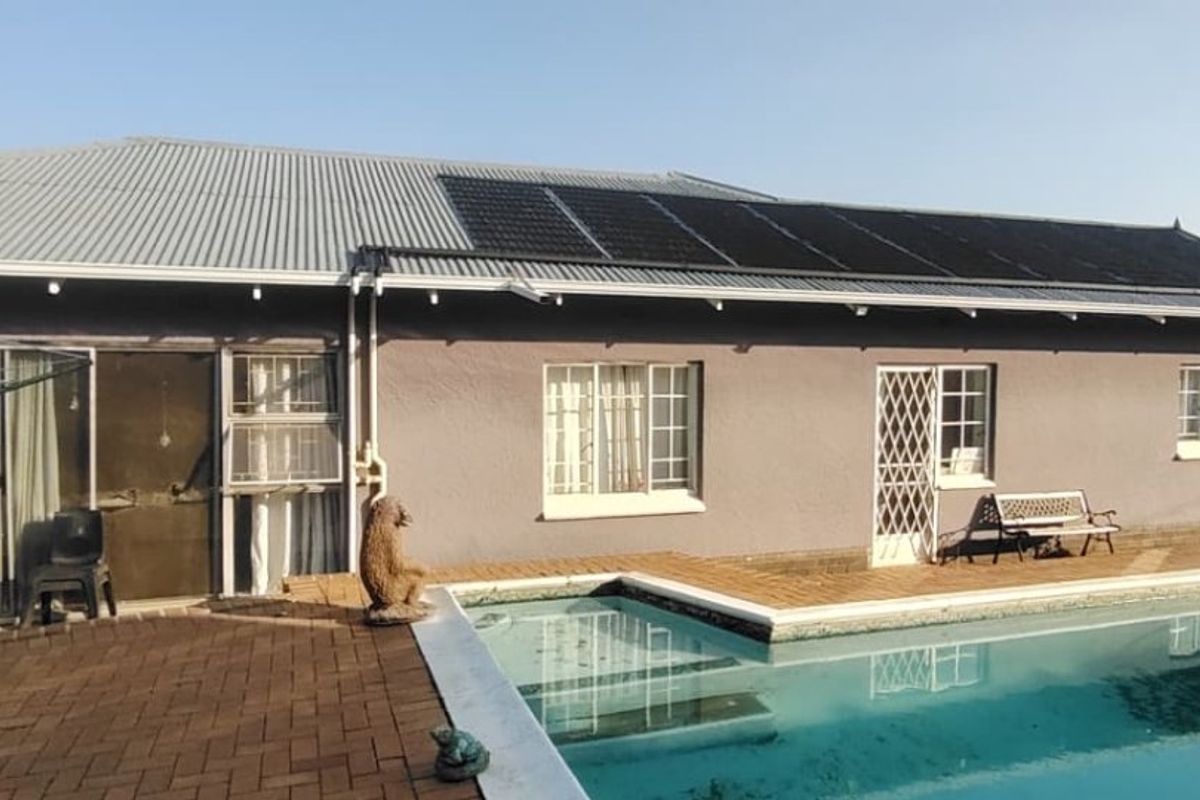 Rear exterior view of the house featuring a swimming pool, paved patio area, and roof-mounted solar panels.