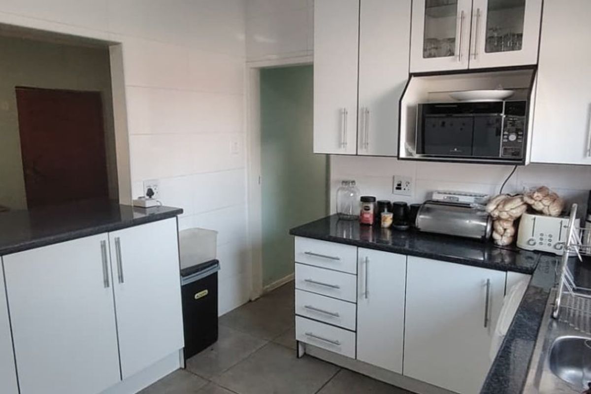 A functional kitchen featuring white cabinetry, dark granite countertops, and a built-in microwave, with an open-plan layout connecting to the adjacent living area.