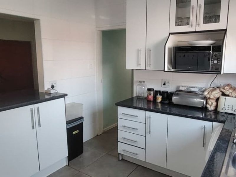 A functional kitchen featuring white cabinetry, dark granite countertops, and a built-in microwave, with an open-plan layout connecting to the adjacent living area.