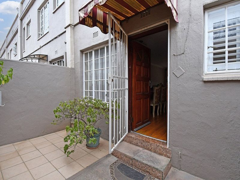 Rear exterior view of the apartment featuring a tiled patio area, security gate, and a covered entrance with a timber door.