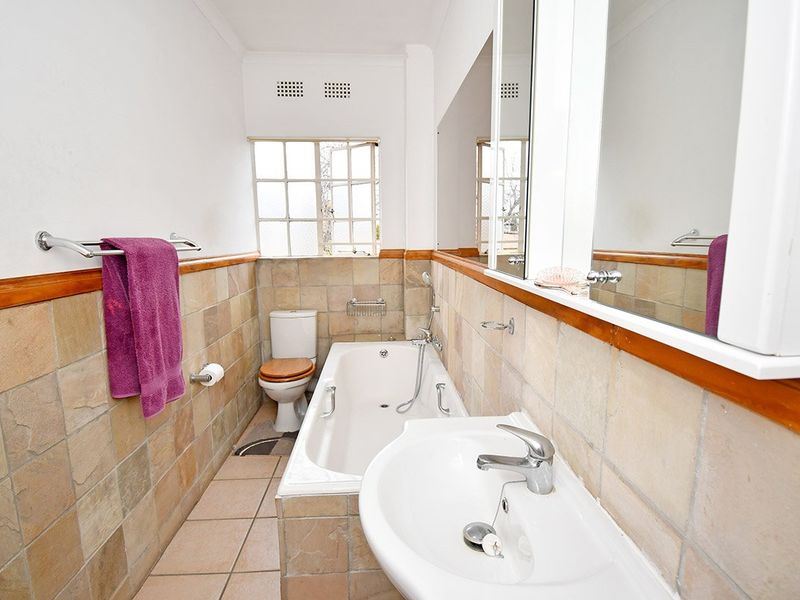 A functional bathroom featuring a bathtub, pedestal basin, toilet, and tiled finishes with a wooden dado rail and large wall-mounted mirror.